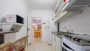 A kitchen with white cabinets, a microwave, a stove, and a dining area with chairs. - Apartments in Beachfront Condo in Itapema - DNL (Itapema)