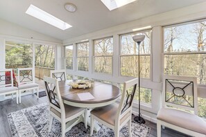 A sunroom with a round table, white chairs, and a large window overlooking a wooded area. - ‘Mountain Golf’ Family Home w/ Deck in Spruce Pine (Spruce Pine)