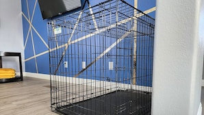 A black metal cage in a room with a blue geometric wall design and a wooden floor. - Large King Bedroom/55" TV/Big fenced yard w games/Dogs welcome/Boat parking (Page)