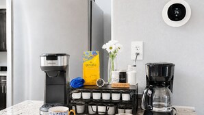 A kitchen with a coffee maker, a box of Gevalia coffee, a coffee mug, a glass of orange juice, and a Nest thermostat. - Large King Bedroom/55" TV/Big fenced yard w games/Dogs welcome/Boat parking (Page)