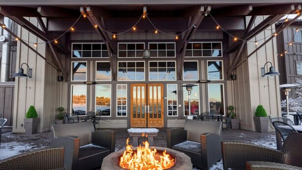 An outdoor seating area with wicker furniture, a central fire pit, and string lights.