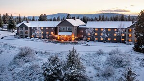 A large, multi-story hotel with a central courtyard, surrounded by snow-covered trees and a mountainous backdrop.