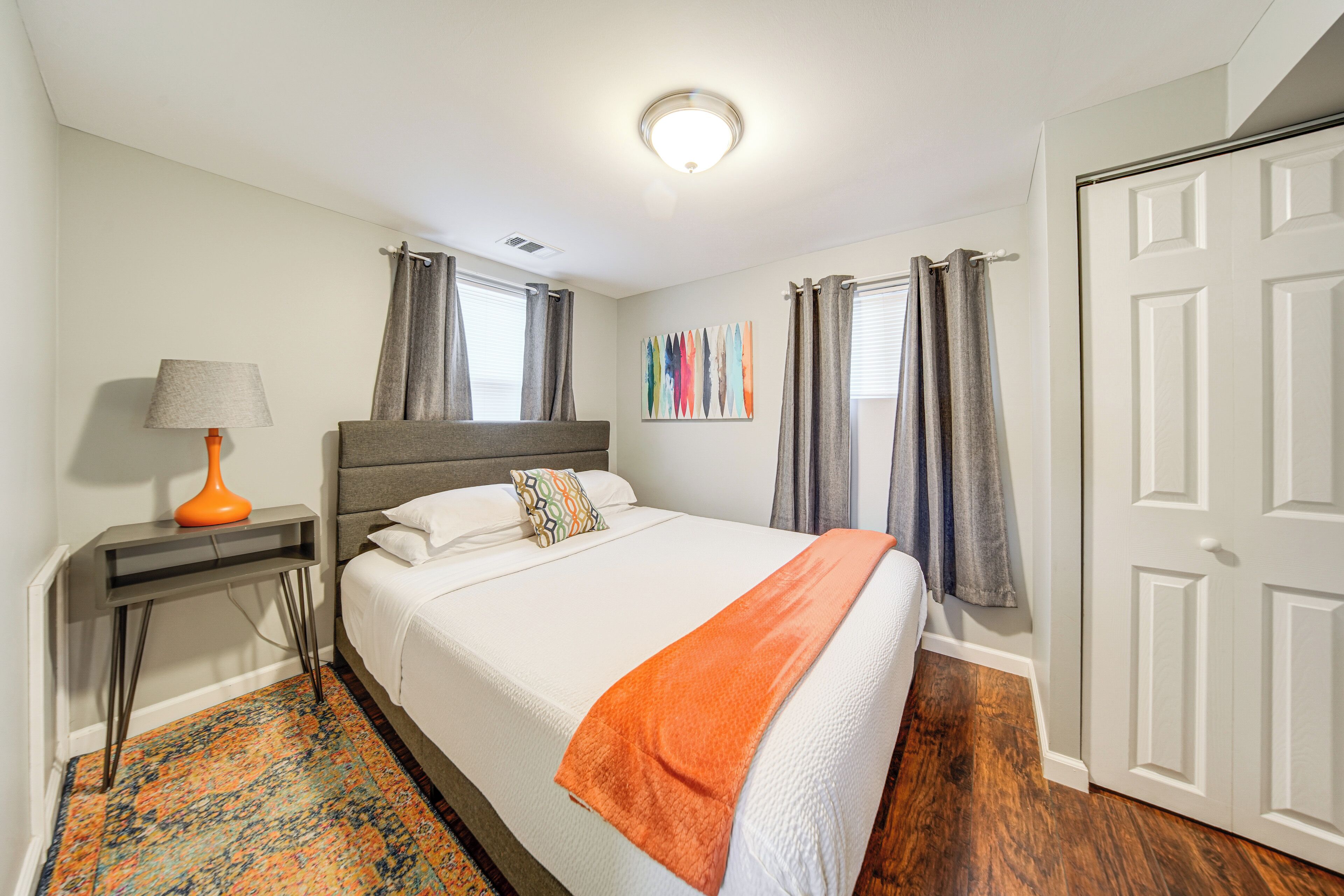 Een netjes opgemaakt slaapkamer met een bed, een nachtkastje met een lamp, een kleurrijk vloerkleed en een deur.