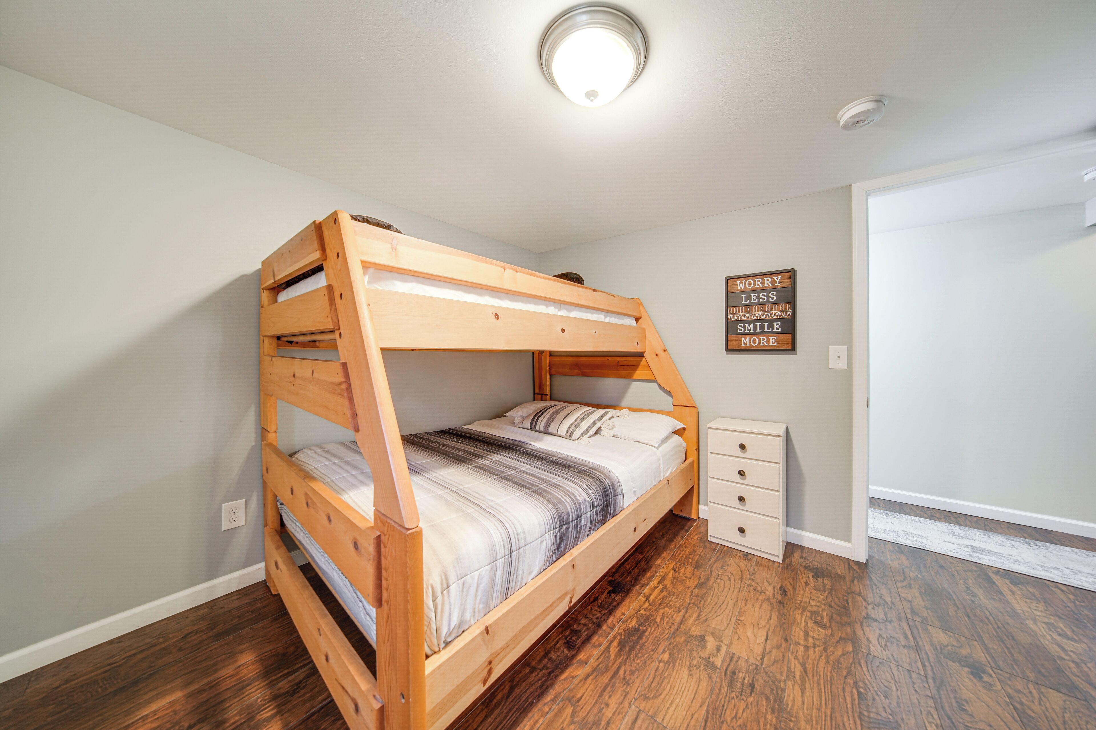 A bunk bed in a room with wooden flooring, a white wall, a small white dresser, and a motivational sign.