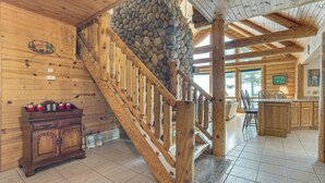 A wooden interior with a stone wall, wooden staircase, and a kitchen area. - On-Site Trails & Private Beach! Lake Huron Retreat (Harrisville)