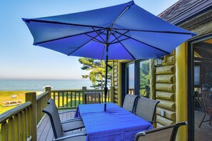 A wooden deck with a table and chairs under a blue umbrella, overlooking a body of water. - On-Site Trails & Private Beach! Lake Huron Retreat (Harrisville)