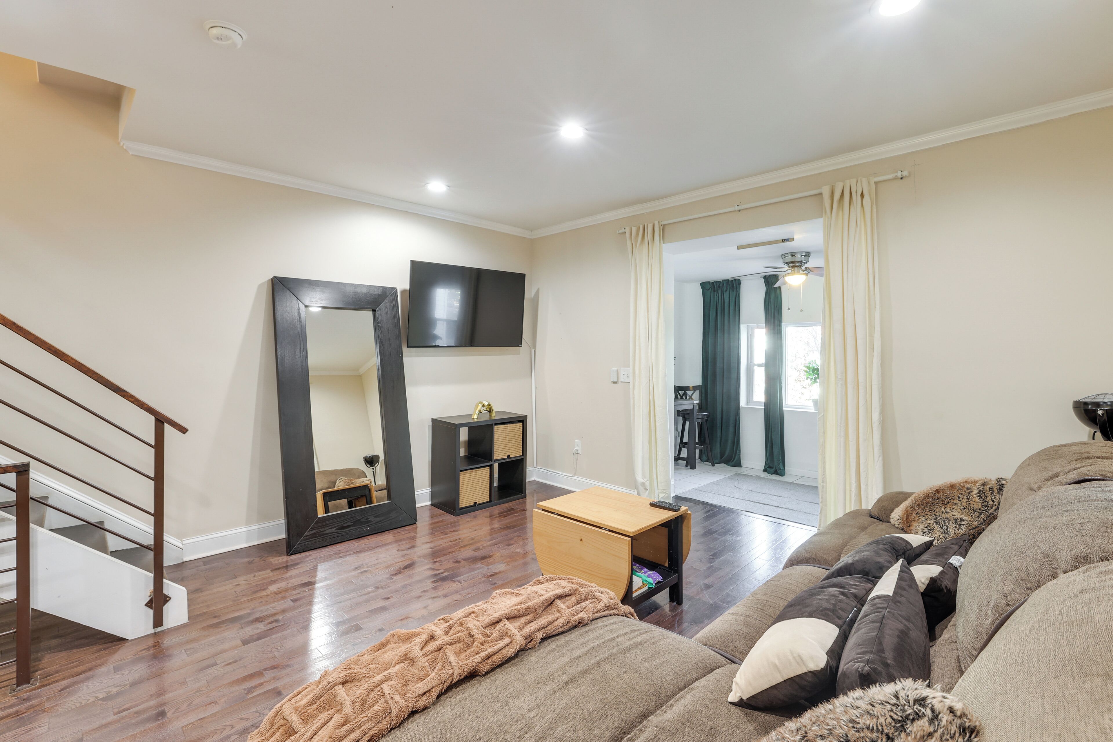 Una sala de estar con una escalera de madera, un televisor de pantalla plana, una pequeña mesa de madera y un sofá con varios cojines.
