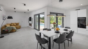 A modern kitchen with a dining area, large windows, and a view of a swimming pool. - Gorgeous home in Sveti Petar u Sumi (Sveti Petar u Sumi)