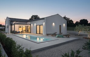 Ein modernes Haus mit Schwimmbad, Sitzgelegenheiten im Freien und einer gut beleuchteten Terrasse.