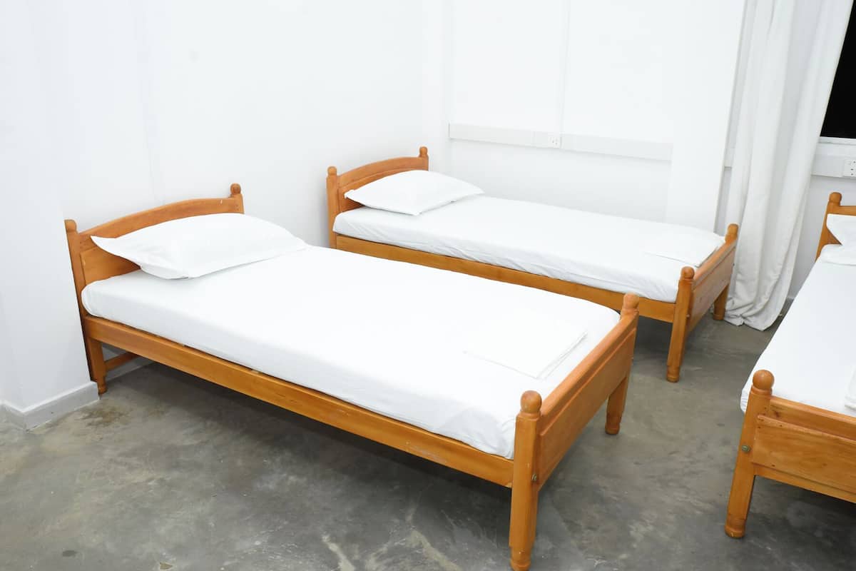 Dos camas individuales de madera con ropa de cama blanca en una habitación con paredes blancas y una ventana.