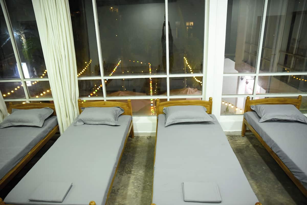 Una habitación con tres camas individuales, cada una con cabecera de madera y ropa de cama gris.