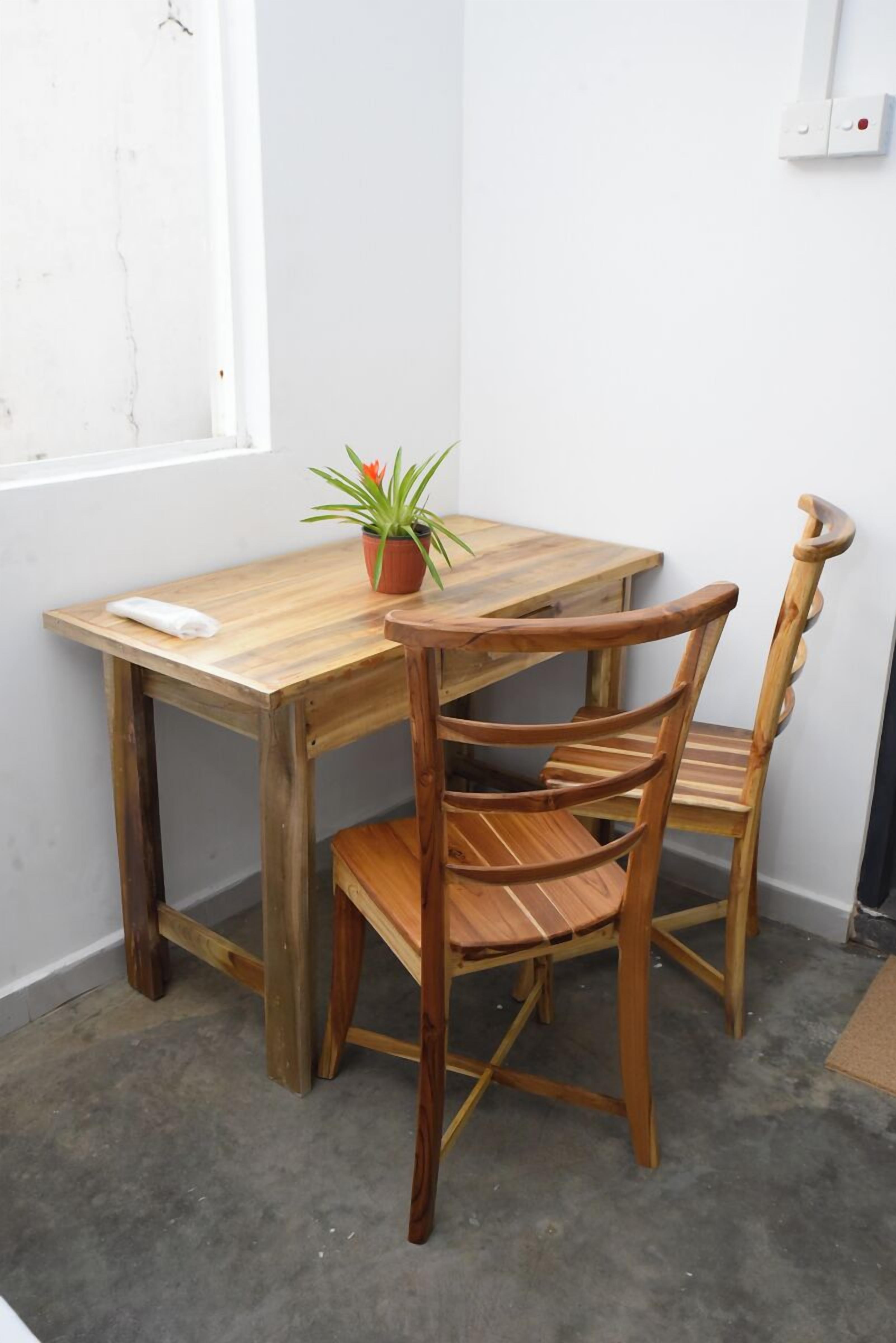 Una mesa de comedor de madera con dos sillas, una planta en maceta y una pared blanca con un ventanal.