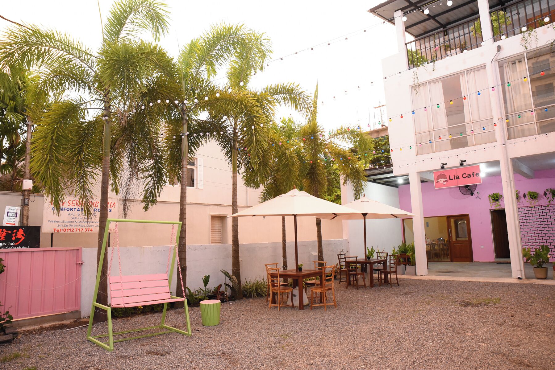 An outdoor seating area with tables and chairs, surrounded by palm trees and string lights.