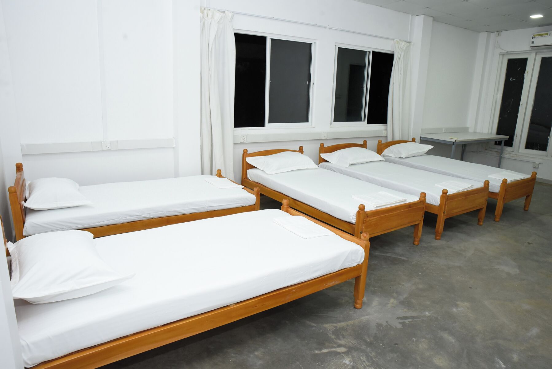 A room with four wooden single beds, white bedding, and a window with curtains.