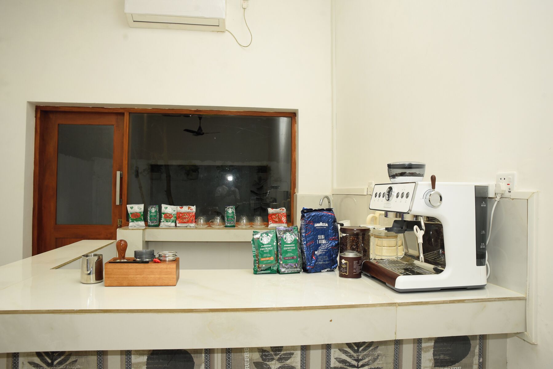 Eine Küchenarbeitsplatte mit einer Kaffeemaschine, Kaffeekapseln und einem Fenster mit Jalousien.