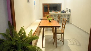Un comedor con una mesa y sillas de madera, una planta pequeña sobre la mesa, y una cocina al fondo.