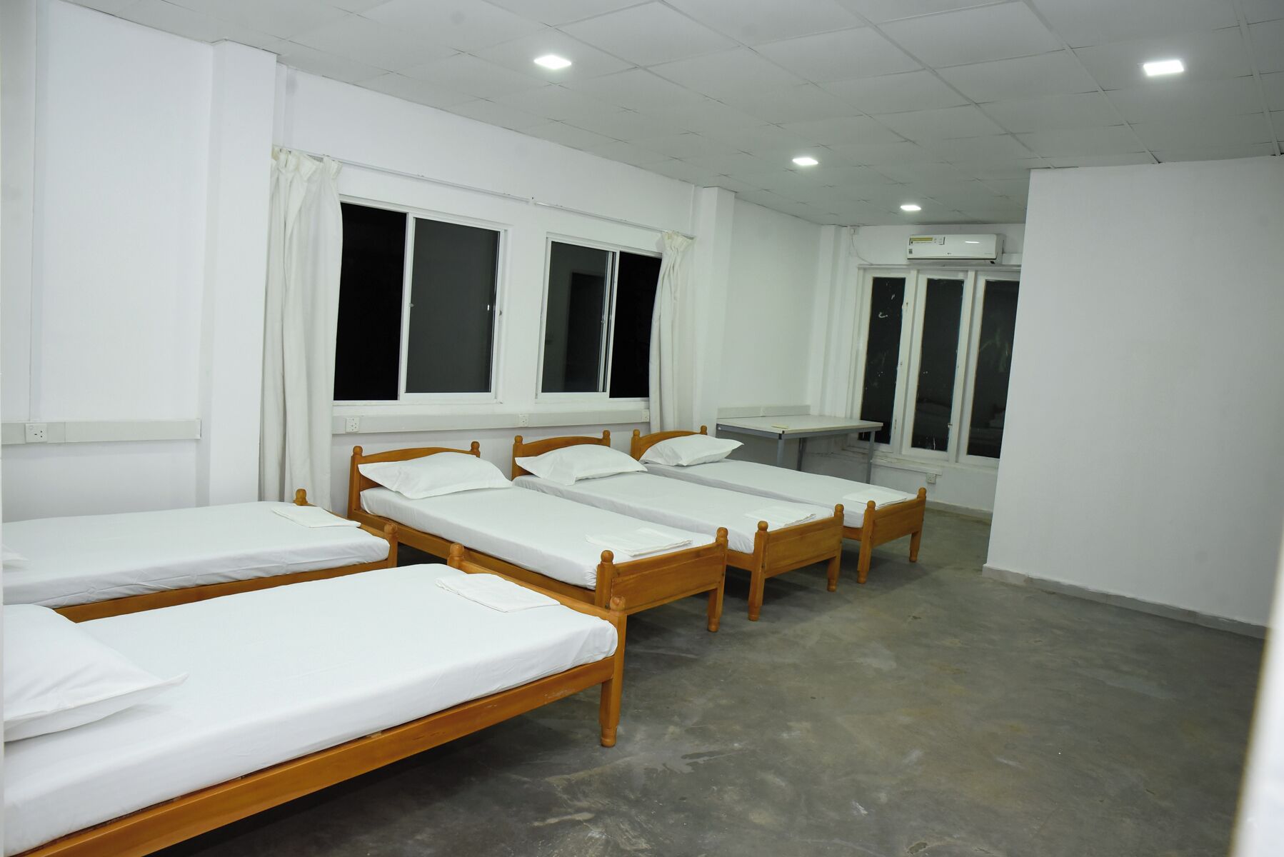 A dormitory room with four wooden beds, white bedding, and a small desk.