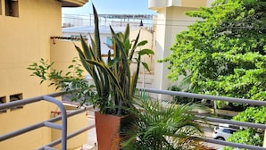 Un balcone con piante in vaso, ringhiera in metallo e vista su un edificio a più piani sullo sfondo.