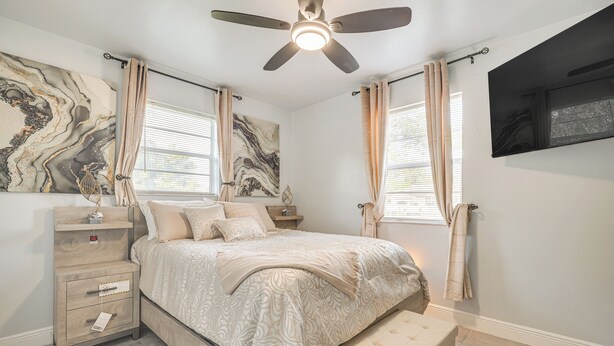 A bedroom with a bed, nightstands, a ceiling fan, and a TV mounted on the wall. - Walk to Shops, Dining & Casino: Dania Beach Home (Dania Beach)