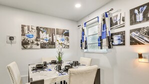 A dining area with a table set for four, surrounded by chairs, with artwork on the walls and a window with curtains. - Walk to Shops, Dining & Casino: Dania Beach Home (Dania Beach)