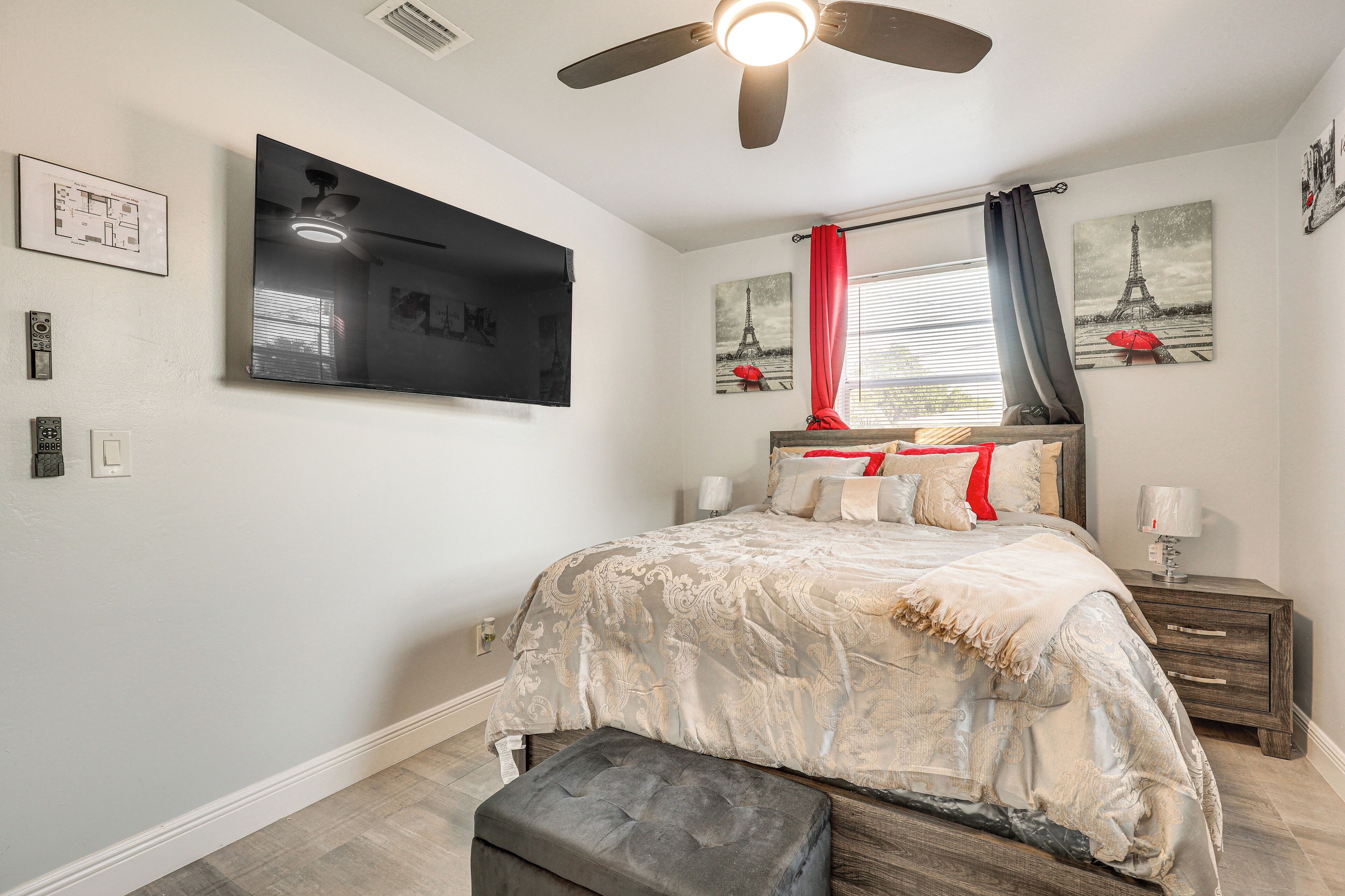 A bedroom with a bed, a ceiling fan, a nightstand, a lamp, and artwork on the walls.