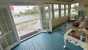 A room with a view of a lake and boats, a white door with a sign, a blue floor, and a beige sofa. - Waterfront Home with Game Room, Kayaks, near beach (Wareham)