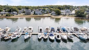 A marina with several boats docked, surrounded by houses and a hill with trees. - Waterfront Home with Game Room, Kayaks, near beach (Wareham)
