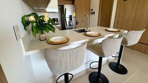 Een moderne keuken met een centraal eiland, twee barstoelen, een spoelbak en een koelkast.