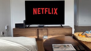 A modern hotel room with a large flat-screen TV displaying the Netflix logo, a wooden cabinet, a round coffee table with a magazine, and a wicker basket with fruits. - Superb 3-bedroom apartment in the heart of Mulhouse (Mulhouse)