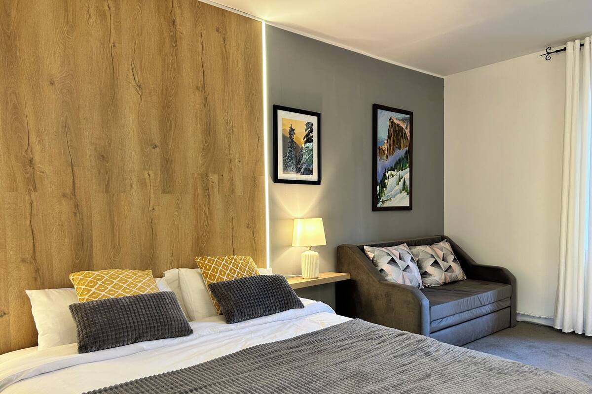 A hotel room with a large bed, a sofa, a nightstand with a lamp, and two framed pictures on the wall.