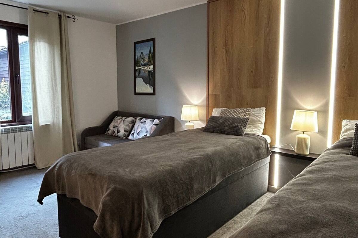 A modern hotel room with two beds, a large window with curtains, a painting on the wall, and a wooden panel on the wall.
