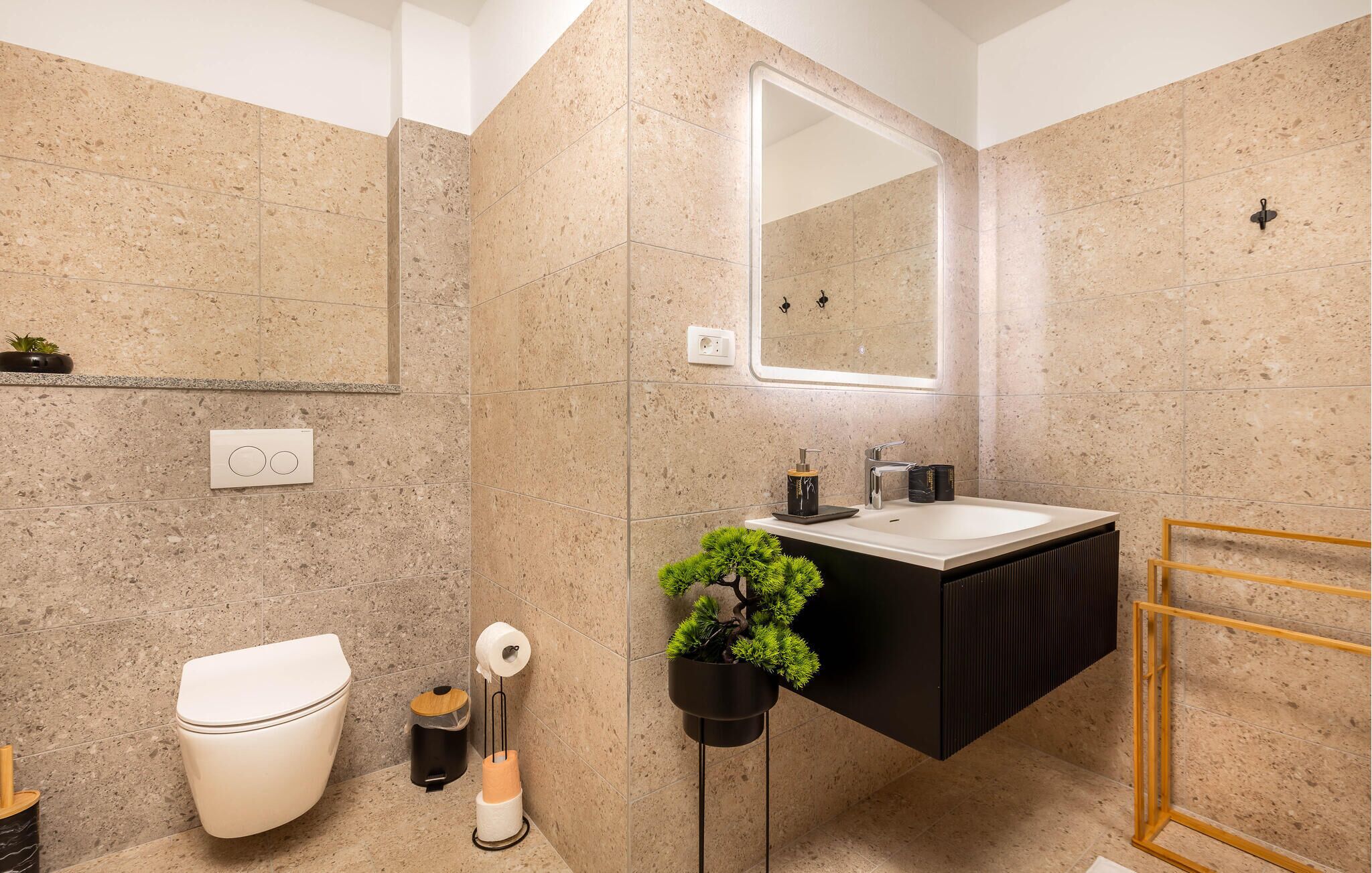 A modern bathroom with a toilet, sink, mirror, and a potted plant.