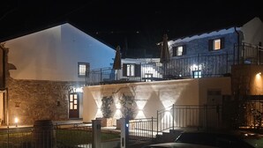 Ein zweigeschossiges Gebäude mit einer Stein-Fassade, einem Balkon mit Sitzgelegenheiten und einem gut beleuchteten Eingang.