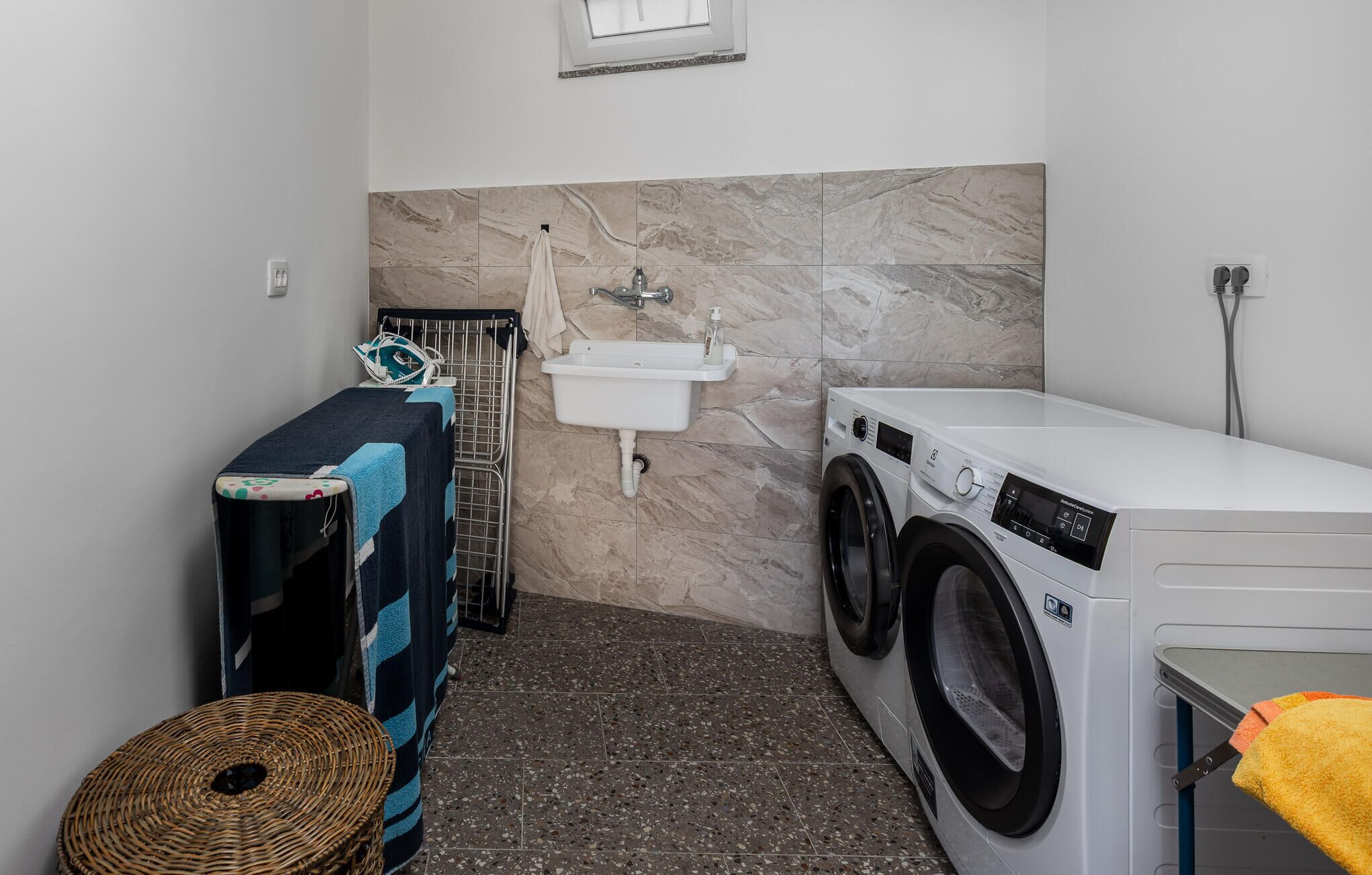 A compact laundry room with a washing machine, a sink, and a drying rack.