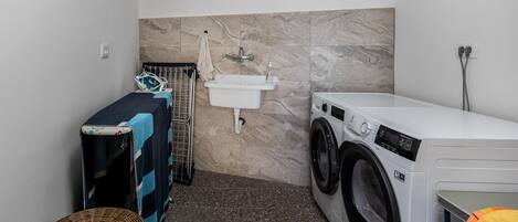 A compact laundry room with a washing machine, a sink, and a drying rack.