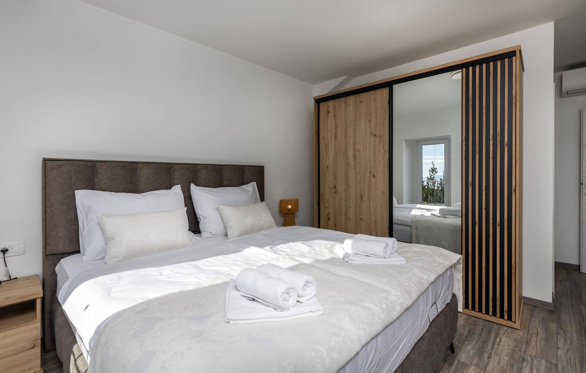 A modern hotel room with a large bed, a wooden wardrobe, and a view of the outdoors.