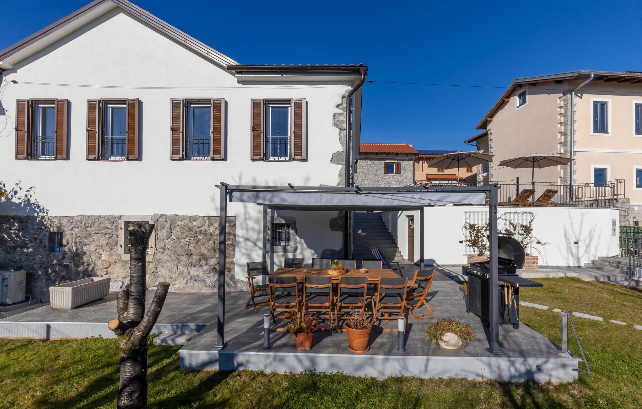 A modern house with a patio area featuring a table and chairs, a barbecue grill, and a covered seating area.