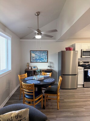 A compact kitchen with a refrigerator, oven, and microwave. A dining table with chairs is set in the center.