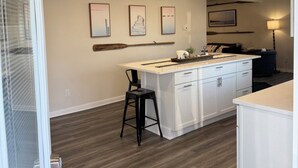 A modern kitchen with white cabinetry, a central island, and a dining area with a black chair. - The Beckman Bungalow - Lakeside 2-bedroom Home (Delavan)