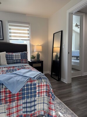 A bedroom with a bed, bedside tables, a mirror, and a door leading to another room.