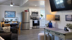 A modern kitchen with stainless steel appliances, a dining area with a table and chairs, a flat-screen TV mounted on the wall, and a ceiling fan. - The Beckman Bungalow - Lakeside 2-bedroom Home (Delavan)