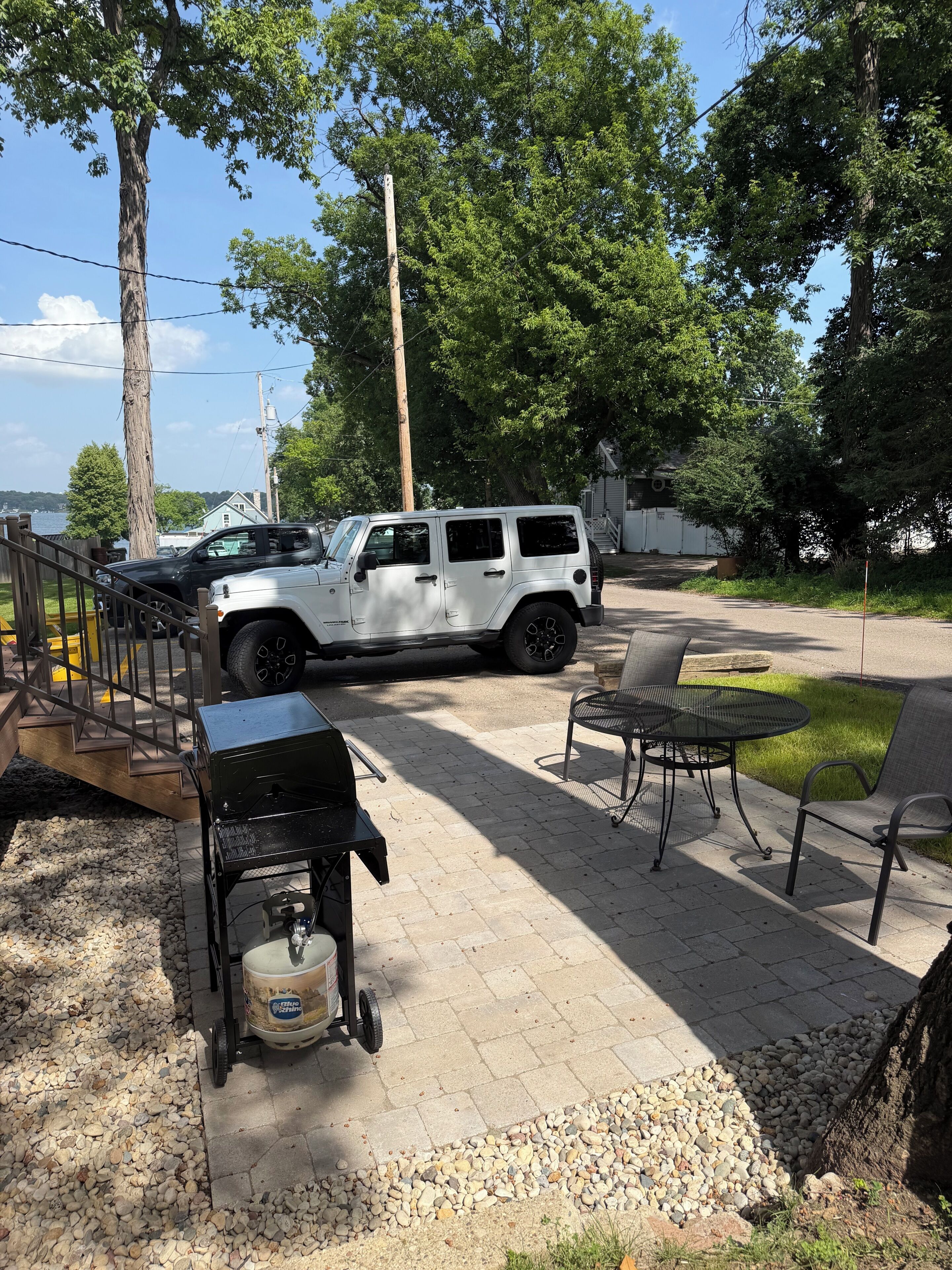 A paved patio with a grill, chairs, and a white SUV parked.
