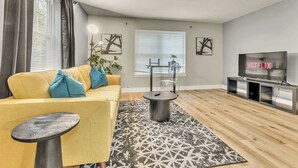 A modern living room with a yellow sofa, a round coffee table, a TV on a stand, and a patterned rug. - The Tanglewood lower suite (Chattanooga)