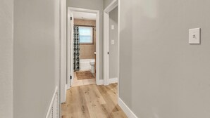 A hallway with a wooden floor leading to a bathroom with a toilet and a shower curtain. - The Tanglewood lower suite (Chattanooga)
