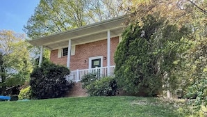 A brick house with a porch, surrounded by a well-maintained lawn and trees. - The Tanglewood lower suite (Chattanooga)