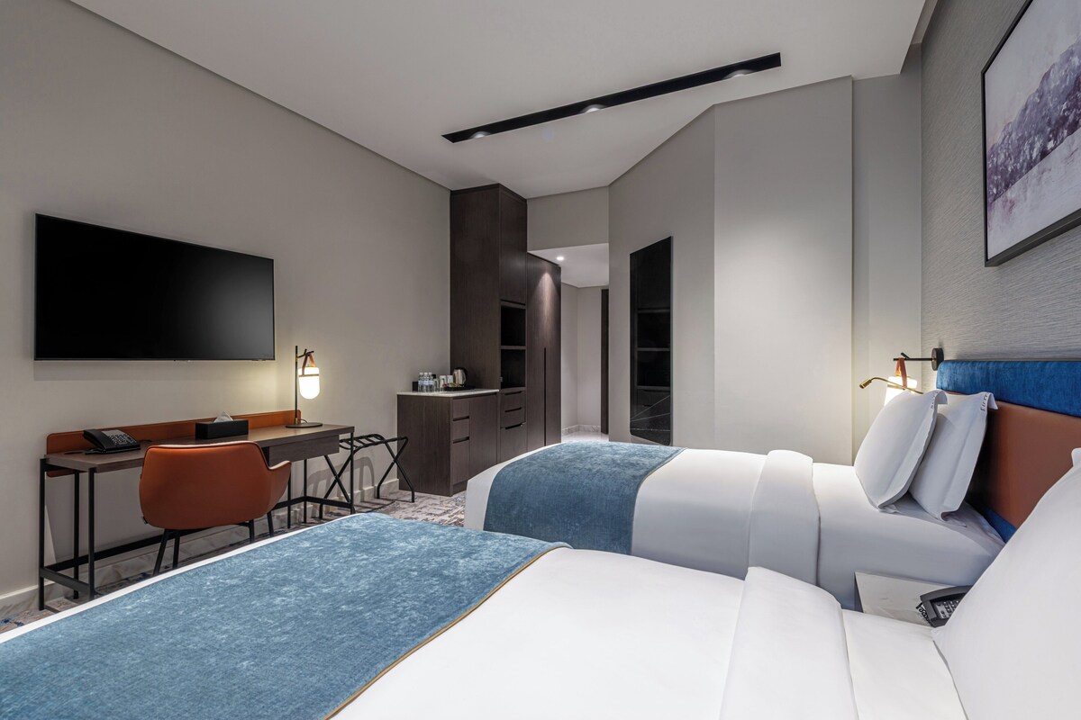 A modern hotel room with a large bed, a desk with a computer, and a flat-screen TV.