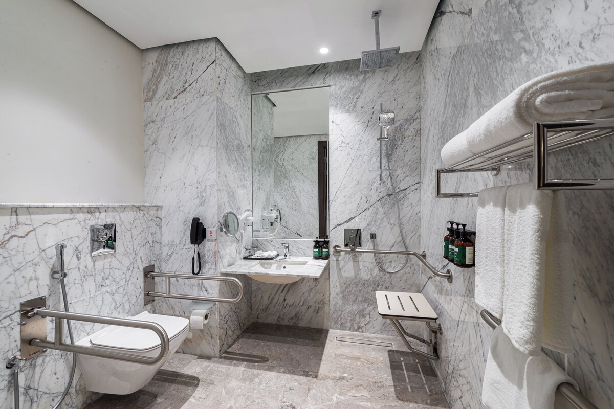 A modern bathroom with a marble wall, a white sink, a toilet, and a shower area.