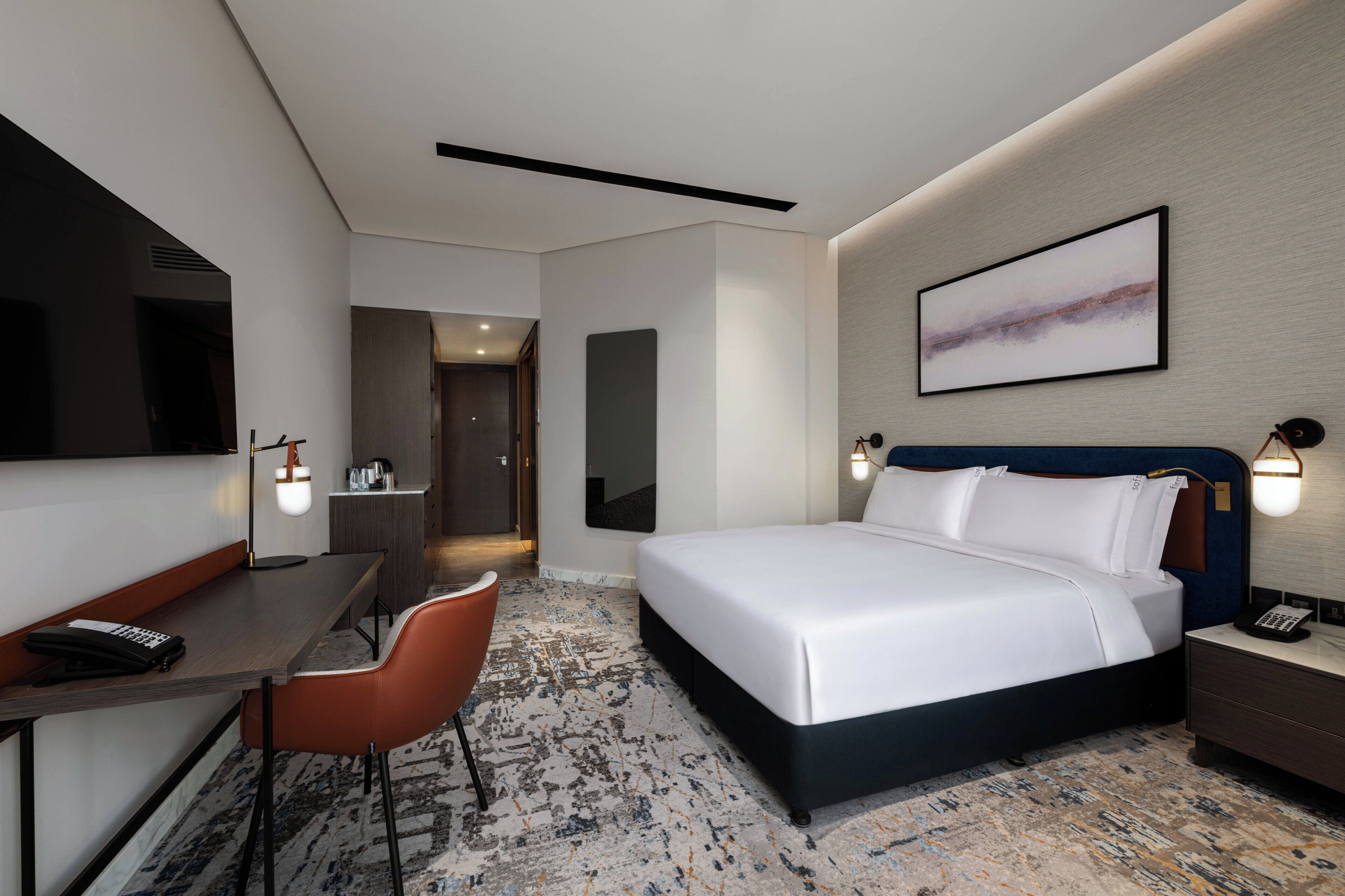 A hotel room with a bed, desk, chair, and a large painting on the wall.