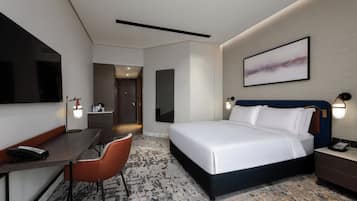A hotel room with a bed, desk, chair, and a large painting on the wall.