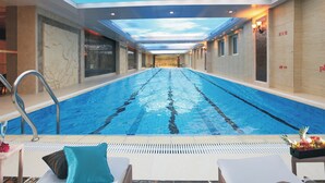 Una piscina con vista despejada al techo y a las paredes, sillas de descanso con cojines y una decoración junto a la piscina.